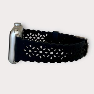 May include: Black silicone Apple Watch band with a delicate floral cutout design.