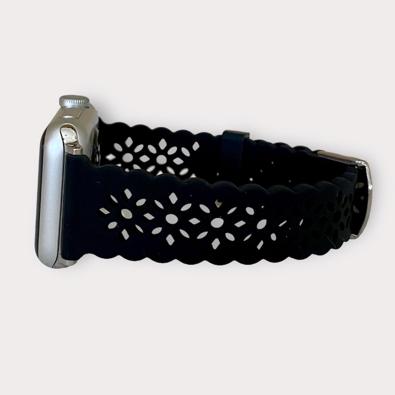 May include: Black silicone Apple Watch band with a delicate floral cutout design.