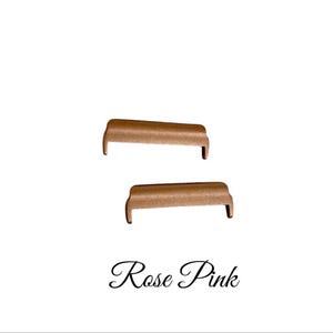 May include: Two rose gold metal watch band connectors. The connectors are shaped like a small couch.