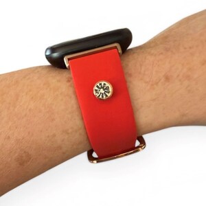 Peut inclure: Un bracelet de montre en silicone rouge avec des &eacute;l&eacute;ments dor&eacute;s et un accent d&eacute;coratif en cristal. Le bracelet est fix&eacute; &agrave; une montre intelligente noire.