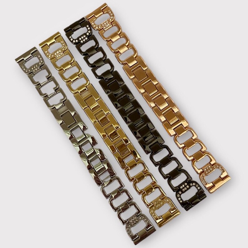 May include: Four watch bands with a metal link design. The bands are in silver, gold, rose gold, and black. Each band has small rhinestones on the links.
