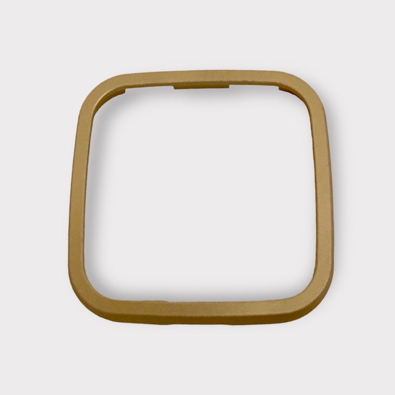 May include: A gold-colored metal frame with a square shape. The frame is smooth and has rounded edges.