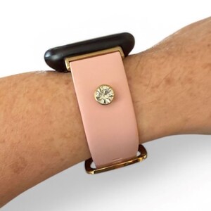 Peut inclure: Un bracelet de montre rose clair avec une boucle dor&eacute;e et un cristal d&eacute;coratif. Le bracelet est fix&eacute; &agrave; un cadran de montre noir.