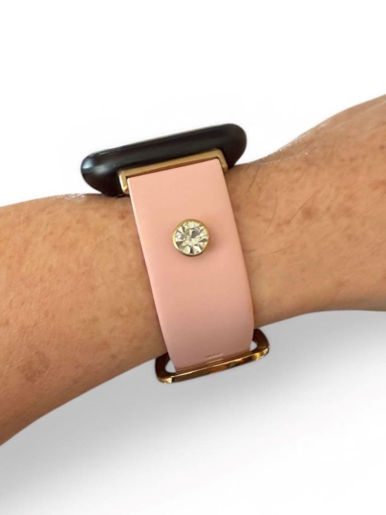 Peut inclure: Un bracelet de montre rose clair avec une boucle dor&eacute;e et un cristal d&eacute;coratif. Le bracelet est fix&eacute; &agrave; un cadran de montre noir.