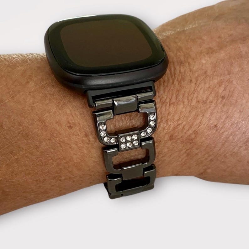 May include: Black smartwatch with a black metal band adorned with clear rhinestones.