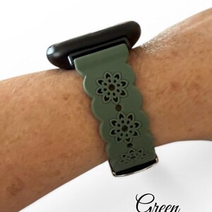 May include: A green watch band with a floral design is attached to a black watch face. The band is worn on a wrist. The word "Green" is written in cursive at the bottom of the image.