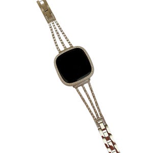 K&ouml;nnte beinhalten: Ein silbernes Armband mit schwarzem Zifferblatt und einer Reihe von klaren Strasssteinen am Rand. Das Armband besteht aus drei Reihen von miteinander verbundenen Metall mit Strasssteinen.