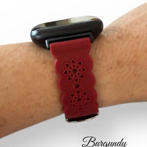 May include: Burgundy-colored smartwatch band with a floral design. The band is attached to a black smartwatch face. The word "Burgundy" is written in cursive at the bottom of the image.