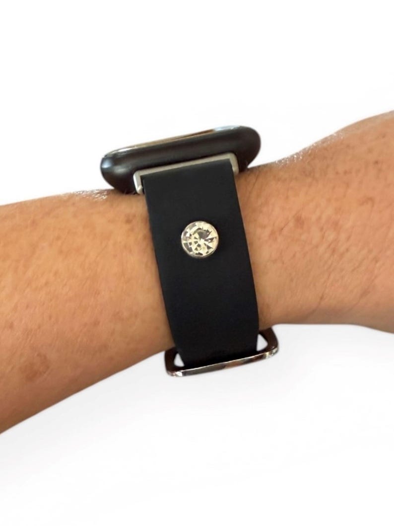 Peut inclure: Bracelet de montre en cuir noir avec une boucle argent&eacute;e et un grand cristal clair. Le bracelet est fix&eacute; &agrave; un cadran de montre fonc&eacute;. Le bracelet est port&eacute; au poignet.