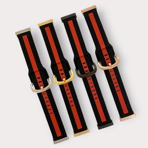 May include: Four black watch bands with red stripes and different colored metal buckles. The bands have a textured surface and are designed for smartwatches.