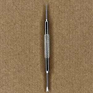 May include: A silver watch band tool with a pointed tip and a textured handle.