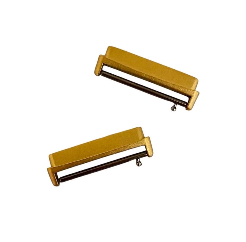 Pu&ograve; includere: Due connettori per cinturino da orologio in metallo color oro con un perno a molla.
