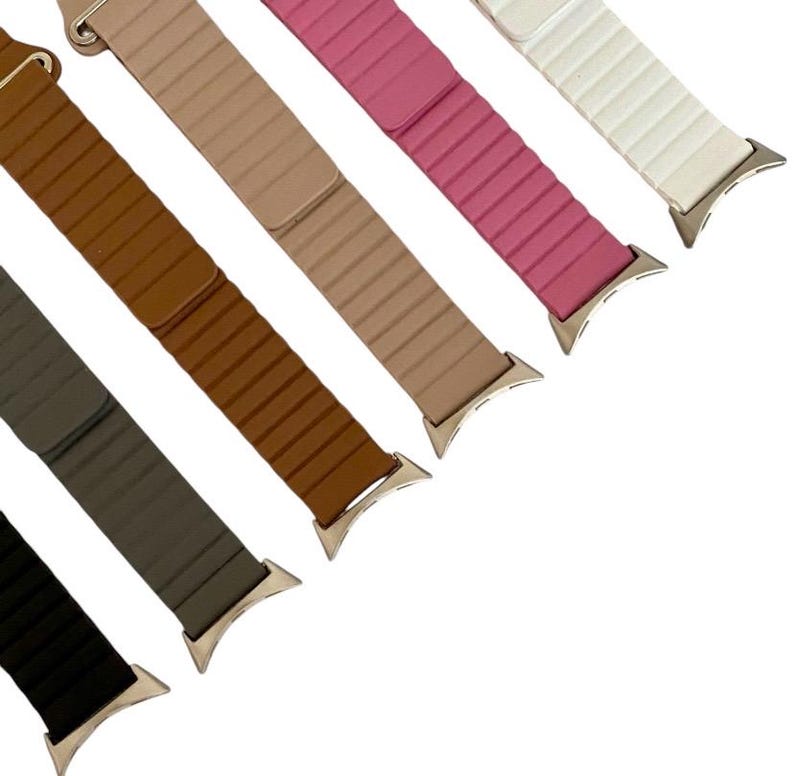 May include: Six different colored watch bands with a silver buckle. The bands are brown, beige, pink, white, gray, and black.