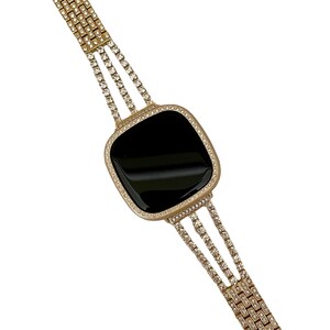 May include: A gold-tone watch band with a black face and a row of clear rhinestones around the edge. The band is made of multiple rows of rhinestones.