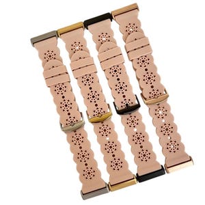 May include: Four light pink watch bands with floral cutouts and various buckle colors: silver, gold, black, and rose gold. The bands have a scalloped edge design and are angled diagonally across the frame.