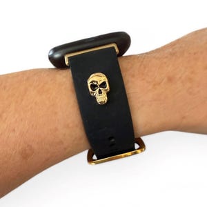 Op de afbeelding: Zwarte horlogeband met een gouden schedelbedel. De band is gemaakt van flexibel materiaal en heeft goudkleurige metalen hardware. De schedelbedel is gecentreerd op de band en voegt een unieke, edgy stijl toe.