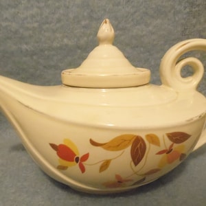 May include: A white teapot with a brown and yellow floral design. The teapot has a curved spout and a lid with a knob on top.