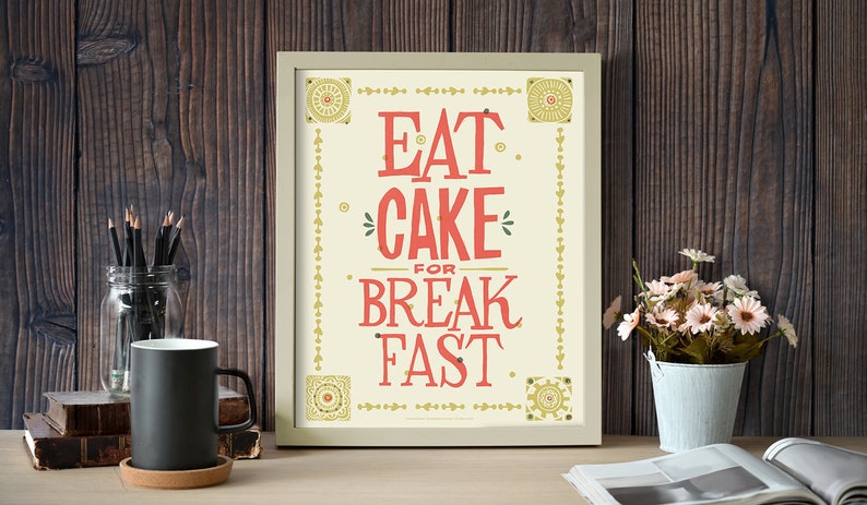 Może przedstawiać: Wydruk w ramie z białym tłem i złotymi akcentami. Wydruk zawiera tekst "Eat Cake for Breakfast." w czerwonych i złotych literach.