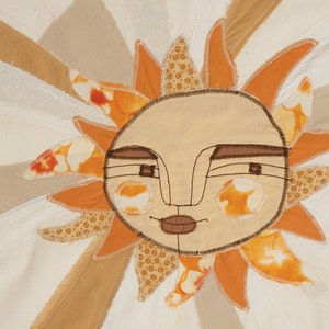 May include: A whimsical sun with a stitched face, made from fabric scraps in shades of orange, brown, and white.
