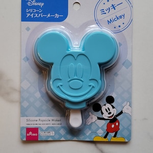 May include: Blue silicone Mickey Mouse popsicle mold with a white stick. The packaging features the Disney logo and the text "Silicone Popsicle Maker" in English and Japanese.
