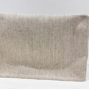 May include: A rectangular clutch bag featuring a light beige and grey herringbone pattern. The fabric has a visible woven texture with a consistent chevron design across the entire surface, finished with clean, straight edges and a structured form.