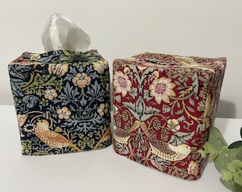 May include: Two square fabric tissue box covers featuring intricate botanical patterns. One cover has a dark navy background with light blue, cream, and tan floral and bird motifs. The second cover has a deep red background with similar floral and bird designs.
