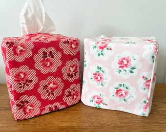 May include: Two floral patterned tissue box covers. One is red with white stripes and white flowers. The other is pink with white flowers and green leaves.