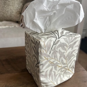 May include: A white tissue box cover with a floral pattern in shades of grey and beige. The cover is made of fabric and has a square shape.