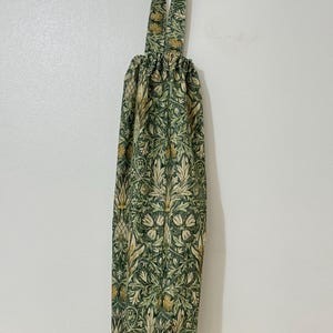 May include: A reusable fabric grocery bag featuring a green and cream floral design. It has a drawstring closure and a loop handle. The bag is made from durable fabric and is designed for repeated use.