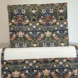 May include: A rectangular fabric cover featuring a dark navy background with a repeating pattern of birds, strawberries, and floral motifs in shades of green, cream, and red. The cover includes a solid white quilted section across the middle.