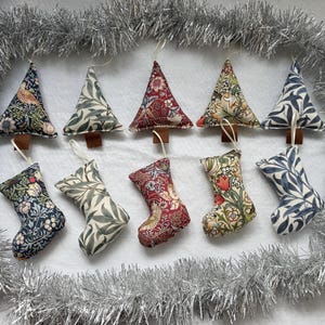May include: A collection of ten fabric ornaments arranged in two rows, featuring five triangular tree shapes and five stocking shapes. Each ornament displays a floral or botanical pattern in various colours including red, blue, green, and cream.