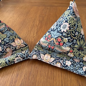 May include: Two triangular fabric items with a dark blue background, featuring a floral and bird pattern in cream, pink, green, and red. They are placed on a wooden surface.
