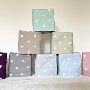 May include: Eight fabric boxes with white polka dots in various colours, including purple, grey, light blue, and pink. The boxes are stacked in a pyramid shape.