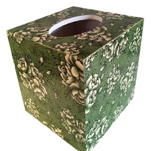 May include: A square tissue box cover with a green background and white floral pattern. The box has a round opening on the top for tissues.