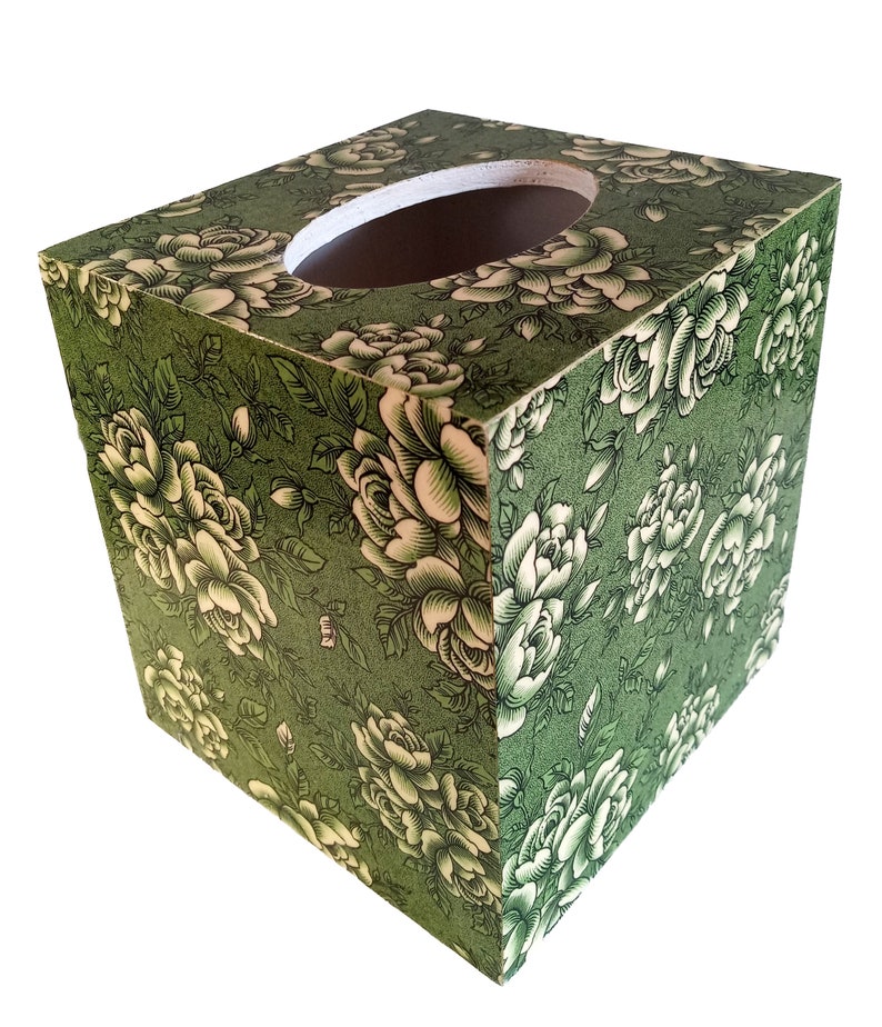 May include: A square tissue box cover with a green background and white floral pattern. The box has a round opening on the top for tissues.