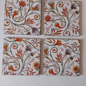 May include: Four square coasters with a floral design. The coasters feature a white background with a repeating pattern of orange, red, blue, and yellow flowers and green vines. The coasters are arranged in a square.