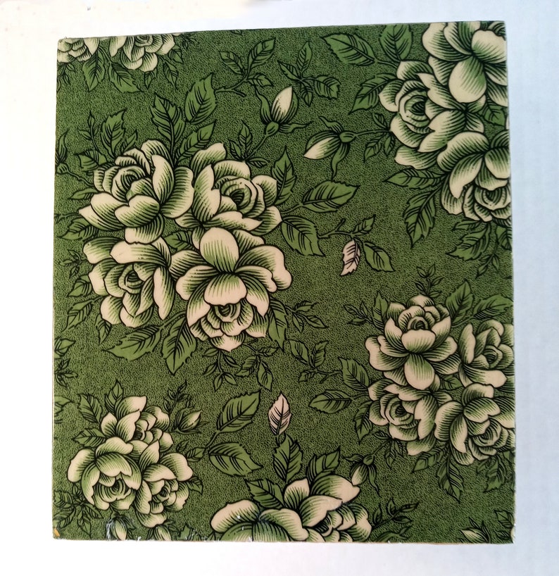 May include: A green square tile with a white floral pattern. The tile features a repeating pattern of white roses with green leaves on a green background.