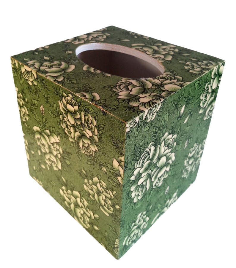 May include: A green tissue box cover with a floral pattern of white roses. The box has a rectangular shape and a cutout for tissues.