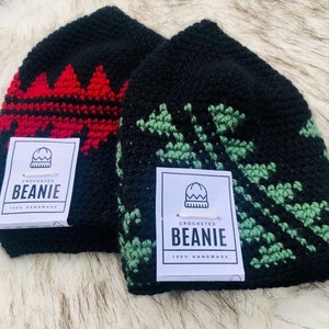 Puede incluir: Dos gorros negros de ganchillo con diseños únicos. Uno presenta un patrón rojo en zigzag, el otro un diseño floral verde. Cada gorro tiene una etiqueta que dice "Crocheted Beanie 100% Handmade."