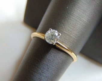 Könnte beinhalten: Ein Goldring mit einem einzigen runden Diamanten in der Mitte.