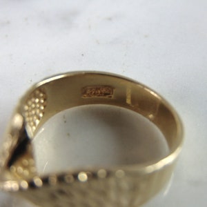 May include: Close-up of the inside of a gold band ring with a textured surface. The ring has the inscription "14K" on the inside.