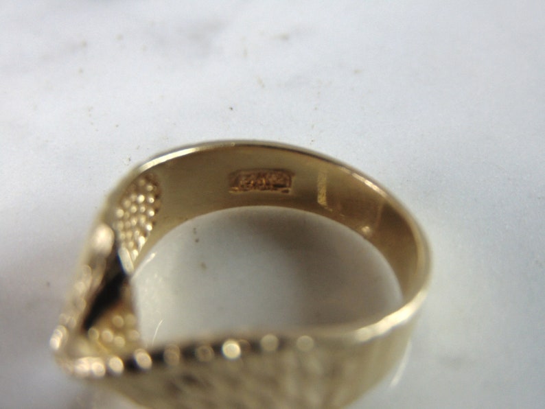 May include: Close-up of the inside of a gold band ring with a textured surface. The ring has the inscription "14K" on the inside.