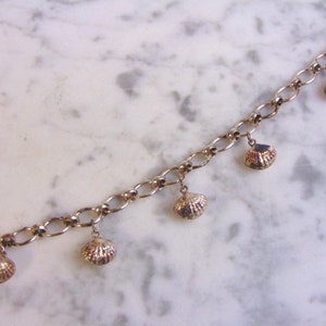 May include: A silver charm bracelet with a chain and multiple shell charms. The bracelet is on a white marble surface.