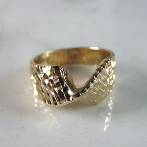 May include: A gold ring with a textured, wavy design. The ring is made of a thick band of metal and has a unique, modern style.