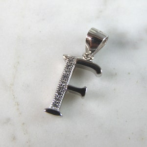 May include: Silver charm pendant in the shape of the letter F, with small clear crystals set into the metal.