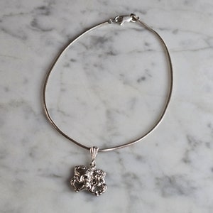 May include: A silver chain necklace with a silver pendant featuring a detailed design of two faces.