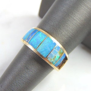 May include: A gold band ring with a blue opal inlay. The opal is set in a series of rectangular shapes.