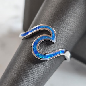 May include: A silver ring with a blue opal wave design.