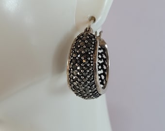Puede incluir: Pendientes de aro de plata con un diseño de piedras negras. Los pendientes están hechos de metal y tienen un acabado pulido.