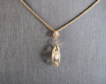 May include: A gold chain necklace with a pendant featuring a single pearl encased in a twisted gold cage.
